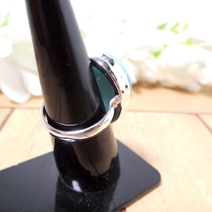 May include: A silver ring with a blue and green oval gemstone. The ring is on a black ring display stand.