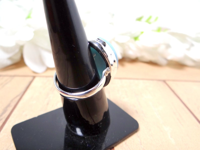 May include: A silver ring with a blue and green oval gemstone. The ring is on a black ring display stand.