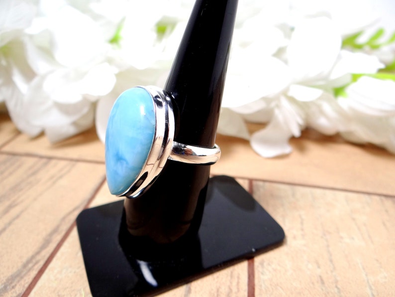 May include: A silver ring with a light blue, pear-shaped gemstone. The ring is on a black ring holder.