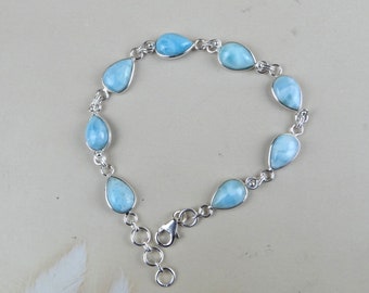 Puede incluir: Un brazalete de plata con una cadena y un cierre. El brazalete está adornado con piedras de color azul claro en forma de lágrima.