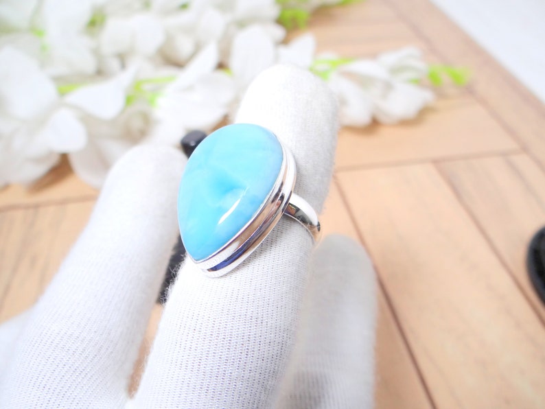 May include: A silver ring with a large, teardrop-shaped blue gemstone. The ring is set on a white fabric background.