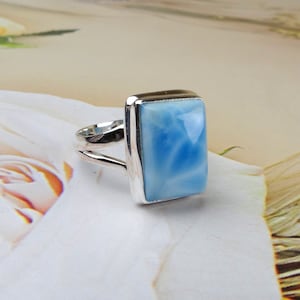 May include: A silver ring with a light blue, square-shaped gemstone. The gemstone has a swirling pattern.