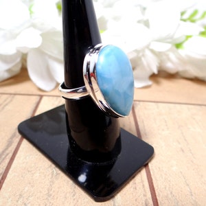 May include: A silver ring with a large, oval-shaped blue gemstone. The ring is set on a black ring stand.