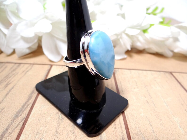 May include: A silver ring with a large, oval-shaped blue gemstone. The ring is set on a black ring stand.