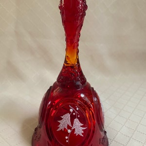 Puede incluir: Una campana de vidrio roja con un diseño grabado en blanco de dos flores. La campana tiene un asa texturizada.