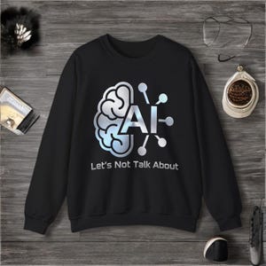 Puede incluir: Sudadera negra con un gráfico plateado y azul de un cerebro y las letras "AI". El texto "Let's Not Talk About" está debajo del gráfico. La sudadera está sobre una superficie de madera.