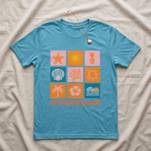 May include: A light blue t-shirt featuring a grid of nine square graphics with a beach theme. The graphics include a starfish, sun, pineapple, seashell, coral, turtle, palm tree, hibiscus flower, and waves. The text "IT'S TAN O'CLOCK" is printed at the bottom.