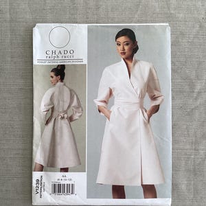 Puede incluir: Un patrón de costura Vogue Patterns de Chado Ralph Rucci, modelo V1239. El diseño es para un vestido cruzado rosa claro con cuello alto y bolsillos. El tamaño del patrón es AA (6-8-10-12).