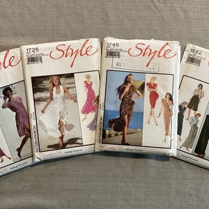 Puede incluir: Cuatro paquetes de patrones Style vintage. Cada paquete presenta ilustraciones de vestidos y otras prendas. Los paquetes están etiquetados con números y la palabra "Style" en escritura roja. El fondo es gris claro.