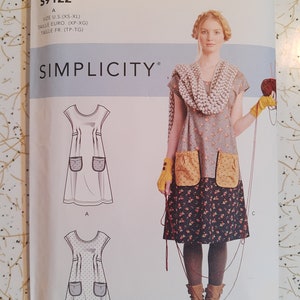 May include: A Simplicity sewing pattern envelope S9122 by Dottie Angel featuring illustrations of a dress with pockets and a photograph of a dress with a grey floral top, a dark floral skirt, yellow pockets, a chunky knit scarf, and yellow fingerless gloves.