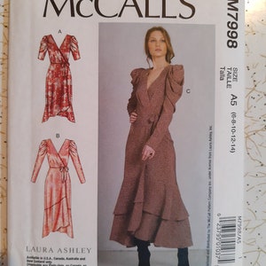 Puede incluir: Un patrón de costura McCall's para un vestido de envoltura con mangas largas y un dobladillo con volantes. El patrón es para las tallas 6-8-10-12-14. El patrón es de Laura Ashley y está disponible en los EE. UU., Canadá, Australia y Nueva Zelanda.