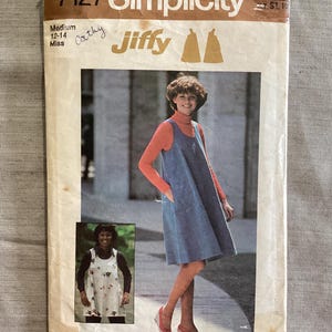 Puede incluir: Un sobre de patrón de costura Simplicity 7127 Jiffy para un vestido de talla mediana 12-14. La portada presenta una fotografía de una persona con un vestido azul sin mangas sobre un cuello alto naranja y una foto pequeña de una túnica.
