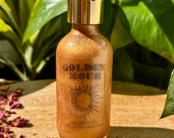 Könnte beinhalten: Eine klare Glasflasche mit Körperschimmeröl und einer goldfarbenen Flüssigkeit. Die Flasche hat eine weiße Pipette und einen goldfarbenen Verschluss. Auf dem Etikett steht "GOLDEN HOUR" mit einem Sonnen- und Monddesign. Der Text "Body Shimmer Oil Feel Your Most Radiant Self" steht ebenfalls auf dem Etikett.