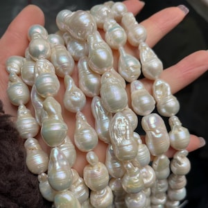 May include: A strand of lustrous, irregularly shaped, white baroque pearls. The pearls have a creamy, iridescent sheen, reflecting hints of pink and green. The organic forms of the pearls create a unique and elegant aesthetic, suitable for jewelry making.