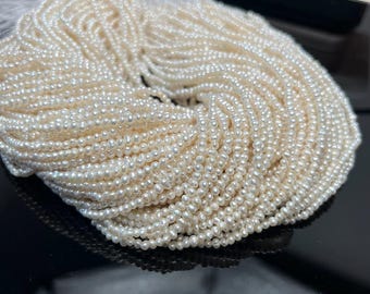 May include: A large bundle of small, off-white pearls. The pearls are strung together, creating a dense, textured appearance. The pearls are round and have a subtle luster, suggesting they are natural. The image is well-lit, highlighting the details of the pearls.