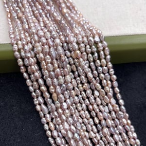 Può includere: Primo piano di numerosi fili di perle ovali in tonalità rosa e bianco. Le perle sono infilate insieme, creando un effetto a cascata. Le perle hanno un aspetto naturale e organico, suggerendo che si tratta di perle d'acqua dolce. Lo sfondo è di colore neutro.