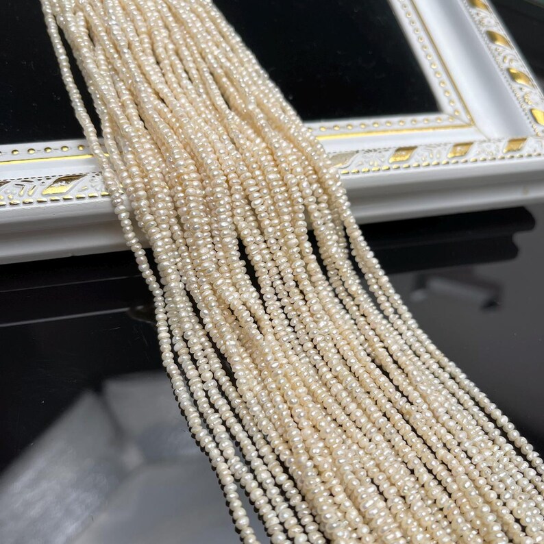 May include: A collection of creamy white, small, seed pearls. The pearls are strung together in multiple strands, creating a cascading effect. The pearls are displayed against a black and white background.