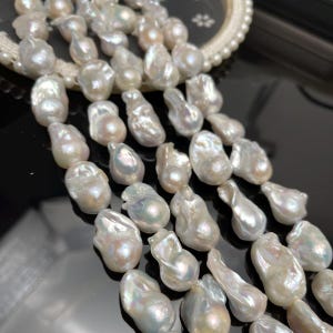May include: Close-up of a strand of lustrous, irregularly shaped white pearls. The pearls have a creamy, iridescent sheen, with subtle variations in color. The pearls are strung together, creating a cascading effect. The background is blurred, focusing attention on the pearls.