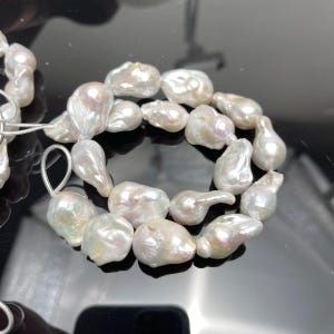 May include: A collection of lustrous, irregularly shaped white pearls. The pearls have a natural, organic form with a pearlescent sheen. The pearls are strung together, suggesting they are intended for jewelry making or a finished piece.