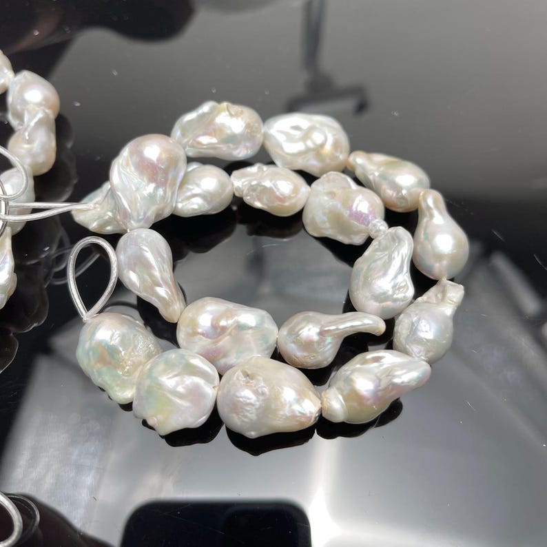 May include: A collection of lustrous, irregularly shaped white pearls. The pearls have a natural, organic form with a pearlescent sheen. The pearls are strung together, suggesting they are intended for jewelry making or a finished piece.