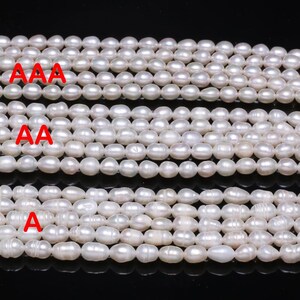 May include: Several strands of white pearls are shown, with varying sizes and shapes. The image displays multiple strands, each graded with the letters "AAA", "AA", and "A" in red. The pearls have a shiny, reflective surface.