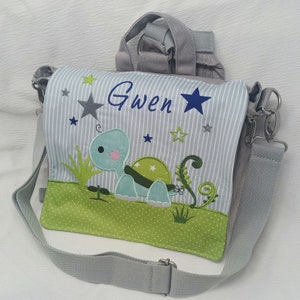 Könnte beinhalten: Eine graue und grüne Stofftasche mit einer blauen und grünen Schildkröten-Applikation. Die Tasche hat einen grauen Trageriemen und einen silbernen Verschluss. Die Tasche ist mit dem Namen "Gwen" und Sternen personalisiert.