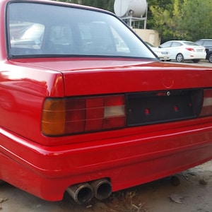 May include: A red BMW 3 Series sedan with a black rear bumper and a black license plate. The car has a chrome exhaust tip and a silver wheel.