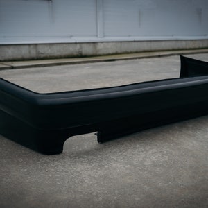 May include: A black plastic car bumper with a smooth, glossy finish. The bumper has a rounded shape and a slight curve at the bottom.