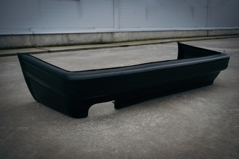 May include: A black plastic car bumper with a smooth, glossy finish. The bumper has a rounded shape and a slight curve at the bottom.