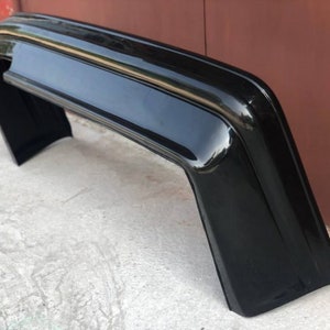 May include: A black plastic car bumper with a smooth, glossy finish. The bumper is curved and has a rounded edge.