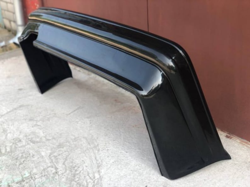 May include: A black plastic car bumper with a smooth, glossy finish. The bumper is curved and has a rounded edge.