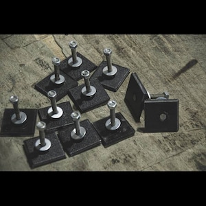 May include: A group of silver screws with black square washers. The screws are arranged in a pattern on a wooden surface.