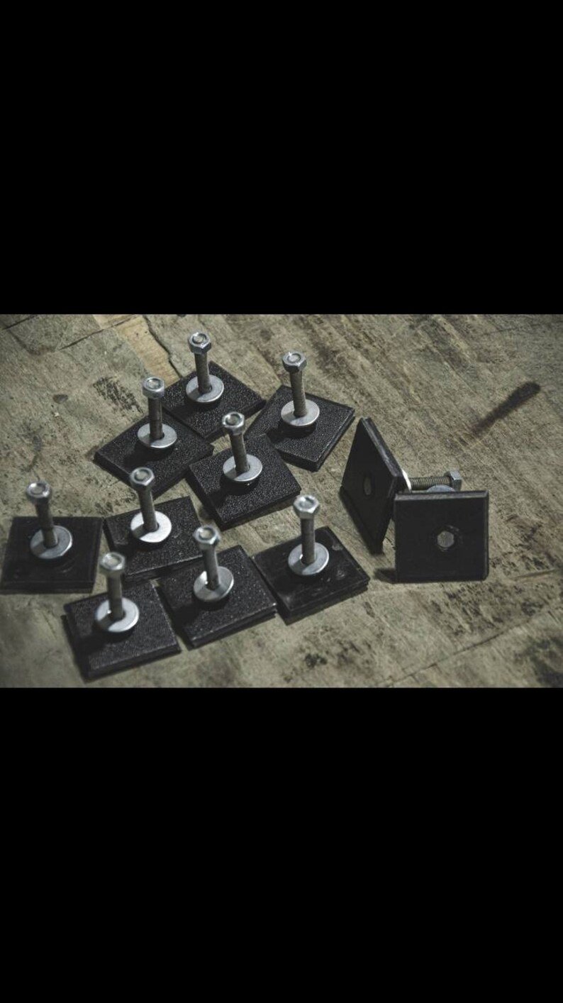 May include: A group of silver screws with black square washers. The screws are arranged in a pattern on a wooden surface.