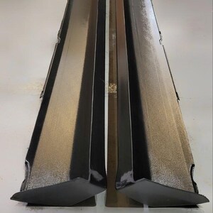K&ouml;nnte beinhalten: Zwei schwarze, kantige Seitenschweller f&uuml;r Automobile, vertikal positioniert und zueinander geneigt. Die Oberfl&auml;chen haben eine gl&auml;nzende Oberfl&auml;che, die das Licht reflektiert. Das Design deutet auf einen Fokus auf Fahrzeug&auml;sthetik und Aerodynamik hin.