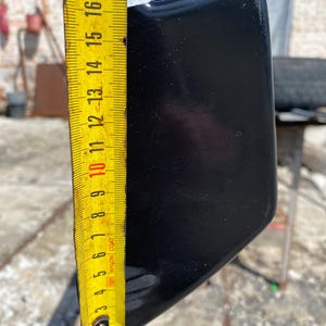 K&ouml;nnte beinhalten: Ein schwarzes, gebogenes Objekt wird mit einem gelben Ma&szlig;band gemessen. Das Ma&szlig;band zeigt eine L&auml;nge von etwa 43 cm an. Das Objekt hat eine gl&auml;nzende Oberfl&auml;che und scheint aus einem harten Material zu bestehen.
