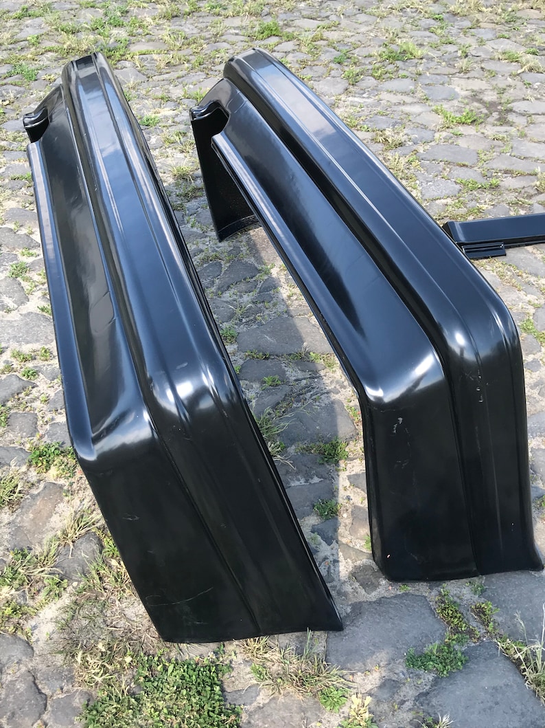 May include: Two black plastic car bumpers, one is lying on its side and the other is standing upright. The bumpers are made of a smooth, glossy material.