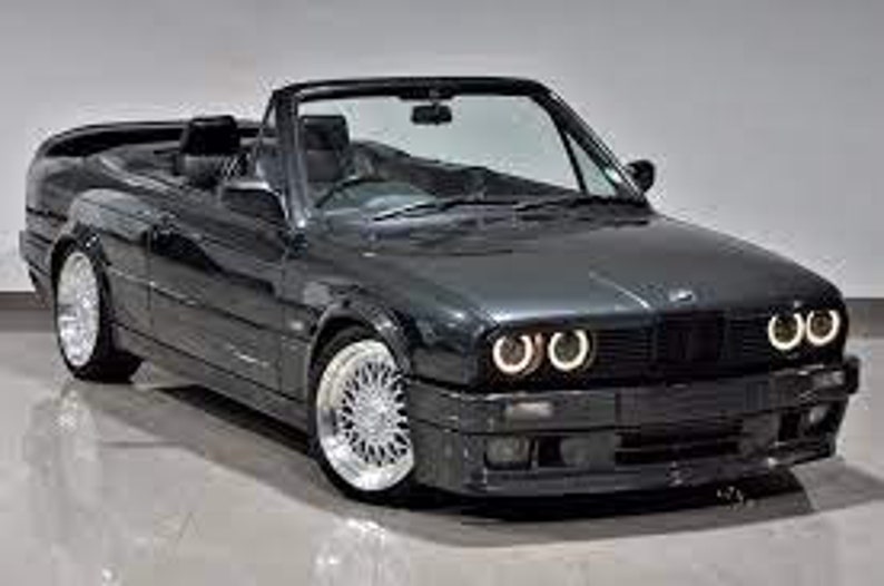 K&ouml;nnte beinhalten: Ein dunkelgraues Cabrio mit schwarzem Innenraum. Das Auto hat ein schlankes Design mit silbernen Felgen und hellen Scheinwerfern. Das Verdeck ist ge&ouml;ffnet und gibt die Sitze und das Armaturenbrett frei. Das Auto scheint in ausgezeichnetem Zustand zu sein.