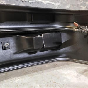 Puede incluir: Un parachoques automotriz negro con un dise&ntilde;o curvo. El parachoques tiene varios recortes rectangulares y est&aacute; asegurado con pernos y una abrazadera. La superficie tiene un acabado brillante, que refleja el entorno.