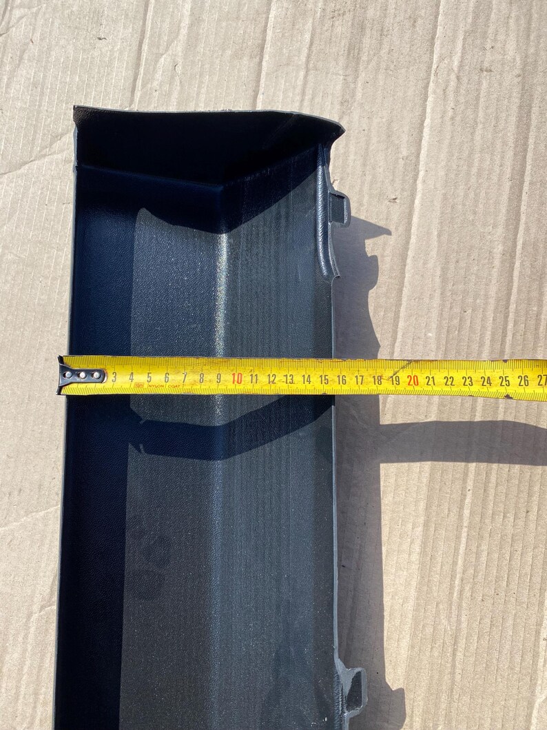 K&ouml;nnte beinhalten: Ein schwarzes Kunststoffteil mit strukturierter Oberfl&auml;che, etwa 25 cm lang, wird mit einem gelben Ma&szlig;band gemessen. Das Teil hat eine rechteckige Form mit gew&ouml;lbter Oberseite und einem kleinen Vorsprung.