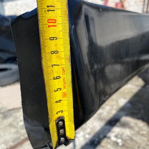 K&ouml;nnte beinhalten: Ein schwarzes, rechteckiges Objekt mit gl&auml;nzender Oberfl&auml;che wird mit einem gelben Ma&szlig;band gemessen. Das Ma&szlig;band zeigt eine Messung von etwa 25 cm an. Das Objekt scheint aus einem haltbaren Material zu bestehen.