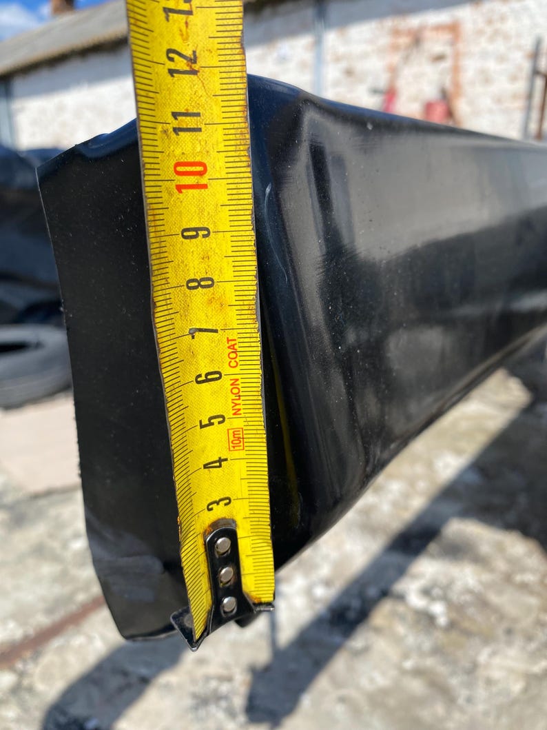 K&ouml;nnte beinhalten: Ein schwarzes, rechteckiges Objekt mit gl&auml;nzender Oberfl&auml;che wird mit einem gelben Ma&szlig;band gemessen. Das Ma&szlig;band zeigt eine Messung von etwa 25 cm an. Das Objekt scheint aus einem haltbaren Material zu bestehen.