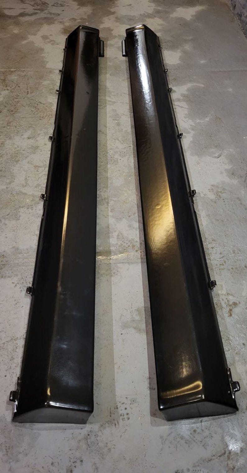 K&ouml;nnte beinhalten: Zwei schwarze, gl&auml;nzende Seitenschweller f&uuml;r Autos. Jeder Schweller ist lang und rechteckig mit einer leicht abgewinkelten Oberkante. Mehrere kleine Clips sind an den Seiten sichtbar. Die Teile sind wahrscheinlich f&uuml;r das &Auml;u&szlig;ere eines Fahrzeugs bestimmt.