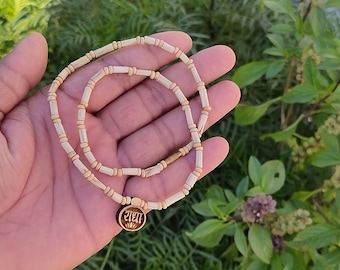 May include: A white wooden beaded necklace with a round wooden pendant featuring the word "शिव" in Sanskrit.