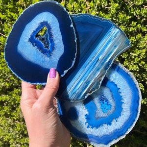 May include: Three blue agate coasters with varying shades of blue and white. Each coaster has a unique pattern of concentric rings, with a central cavity. The coasters are approximately 4 inches in diameter.