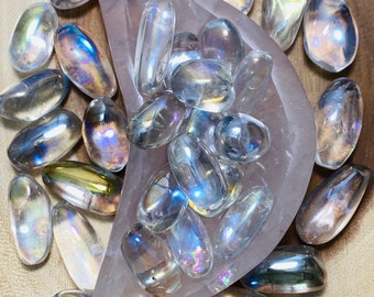 May include: A collection of iridescent clear quartz tumbled stones in a pink crescent-shaped dish. The stones are smooth and have a rainbow sheen.