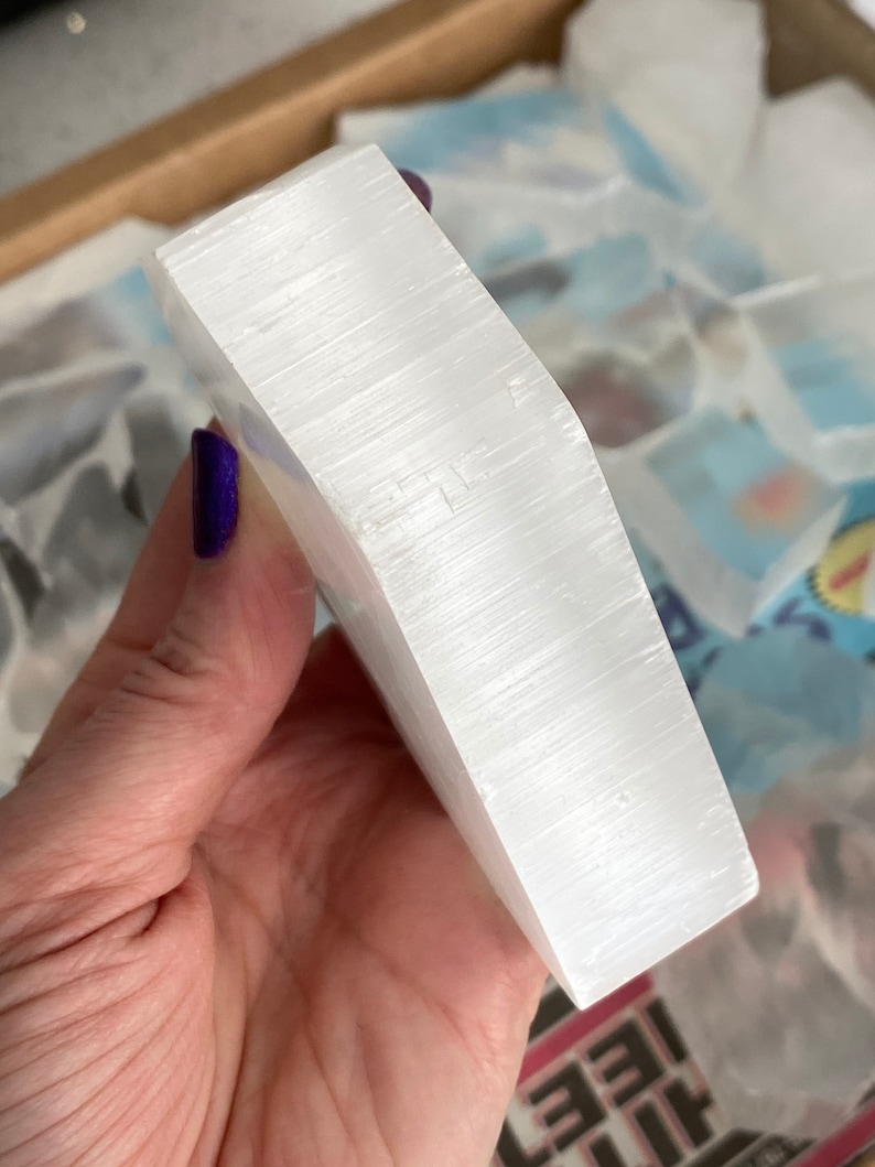 May include: A white selenite crystal slab with a smooth, polished surface. The crystal is held in a hand, showcasing its size and shape.