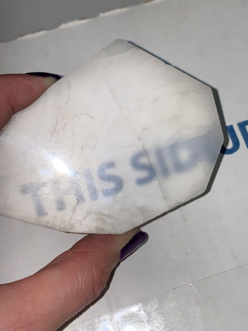May include: A white, opaque, irregularly shaped stone with the words "This Side" written on it in blue ink.