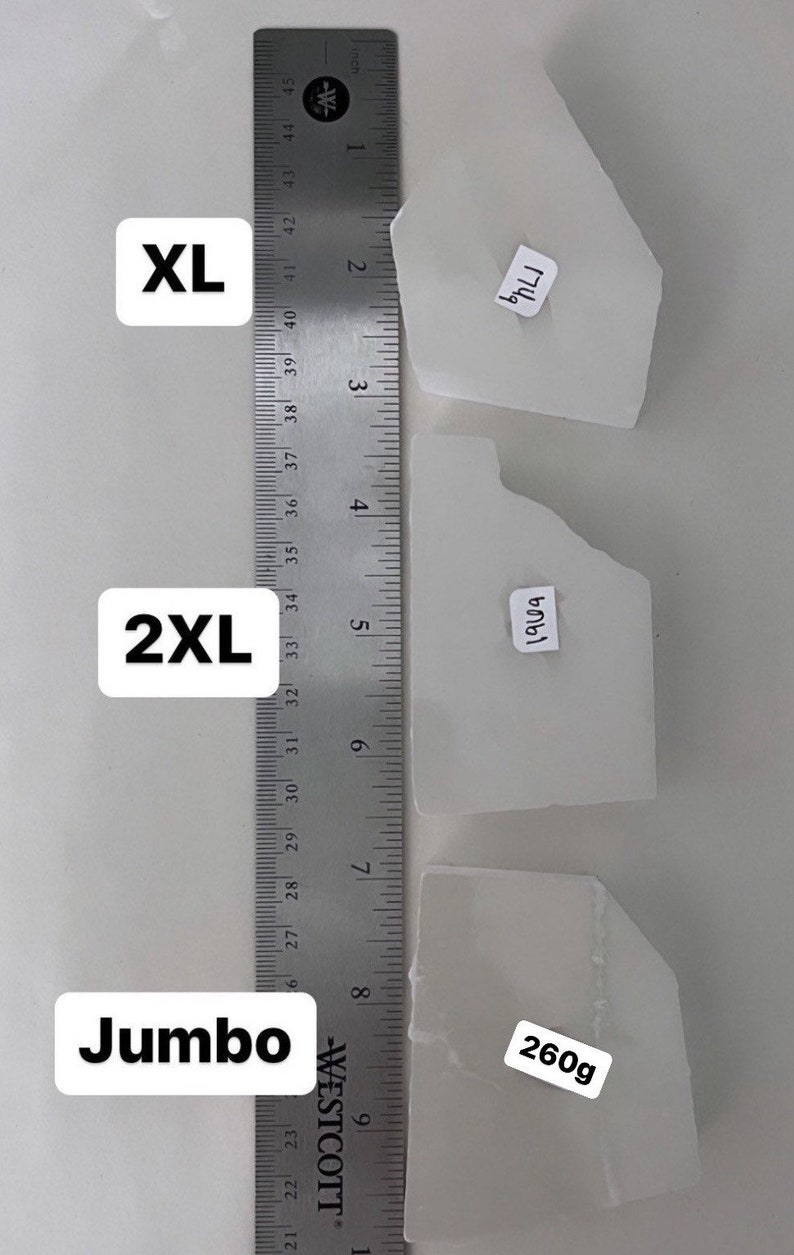May include: Three white, rectangular pieces of selenite crystal, labeled "XL", "2XL", and "Jumbo". A ruler is shown for size reference. The largest piece is labeled "260g".