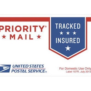 May include: A white rectangular label with red and blue text and graphics. The label reads "PRIORITY MAIL" and "TRACKED INSURED" with the United States Postal Service logo. The text "For Domestic Use Only" is also present.