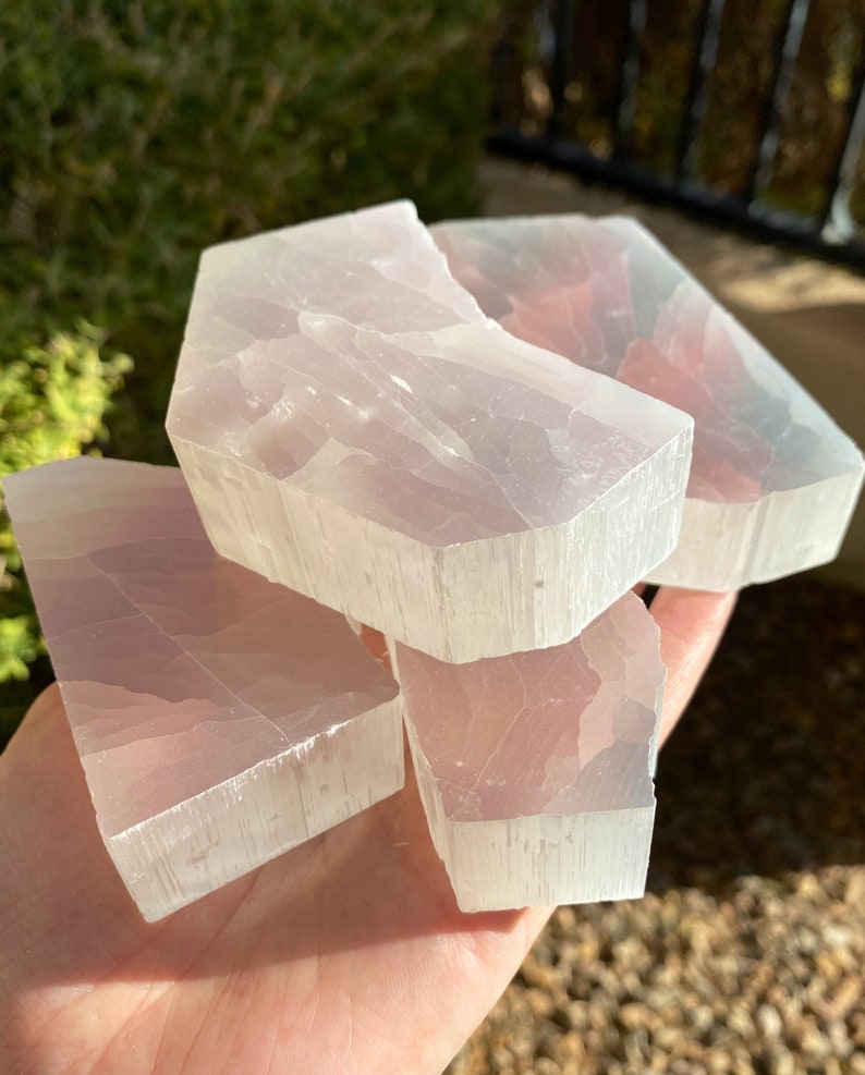 May include: Four pieces of selenite crystal, each with a translucent white color and a striated texture. The crystals are stacked on top of each other, with the top crystal partially broken.